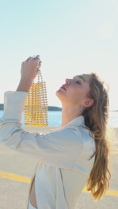 Gold beaded mini handbag by Thalie Paris showcased in motion during a seaside editorial shoot.